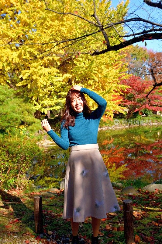 年轻的日本女人欣赏秋天的树叶，旋转她的头发，跳，跳舞和摆姿势