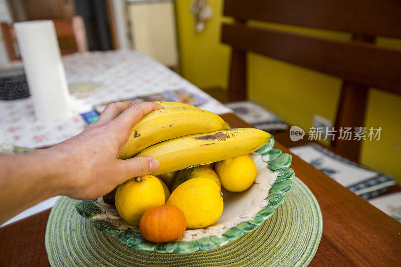 年轻人从家里的水果盘里拿香蕉