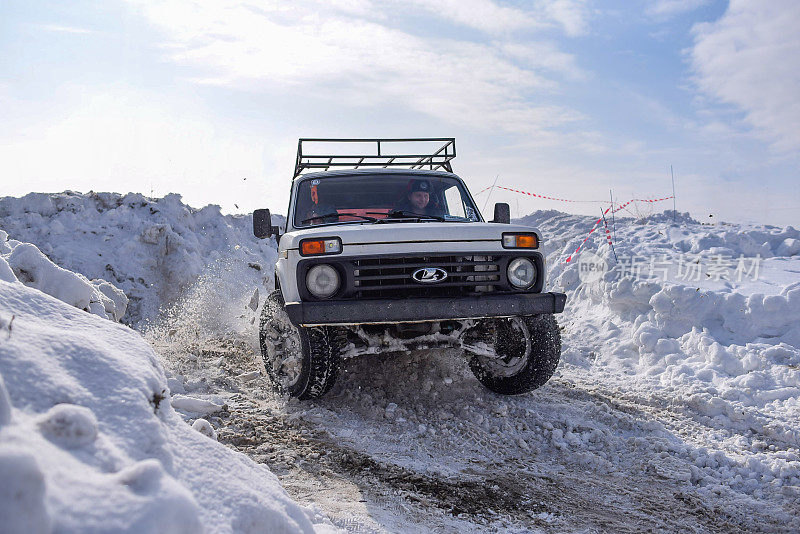 俄罗斯越野车“拉达尼瓦4x4”在冬天的雪天里快速行驶，一名兴高采烈的司机戴着一顶带耳罩的帽子。