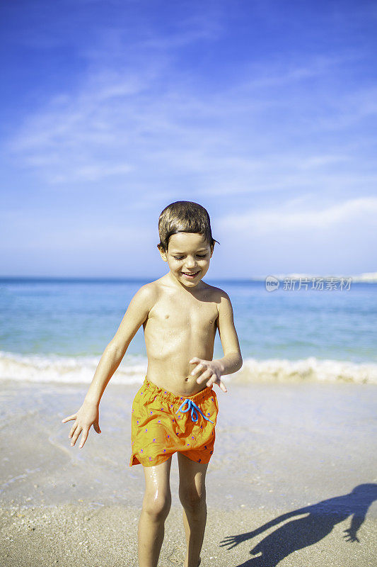 小男孩在海滩上玩，被海浪溅起水花。阳光明媚的夏日在迪拜股票照片