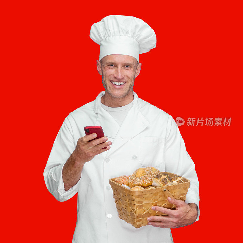 白人年轻男性面包师站在有色背景下穿着裤子拿着长棍面包发短信