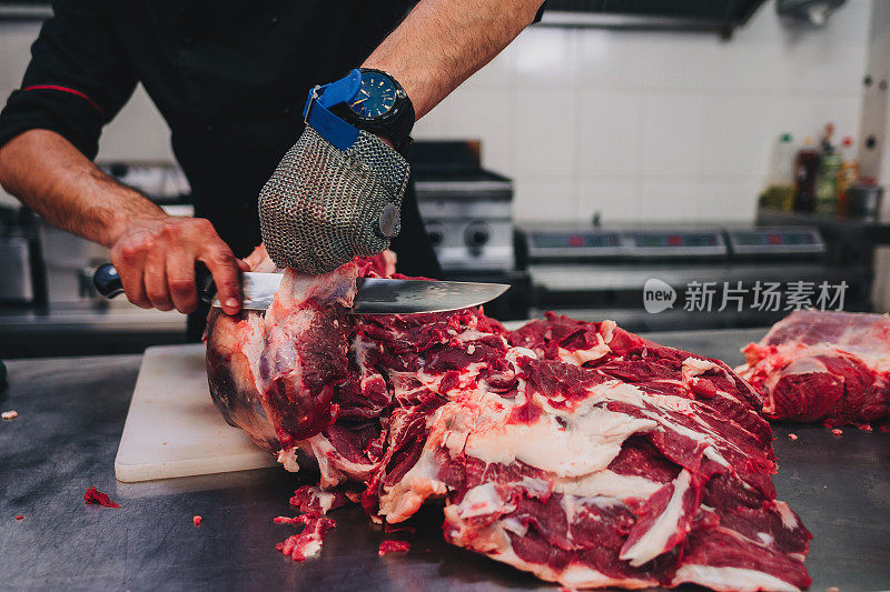 男屠夫在餐厅厨房用刀切生牛肉