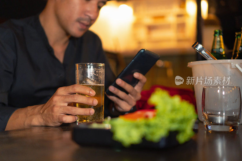 特写，亚洲男子使用智能手机和品脱玻璃杯。