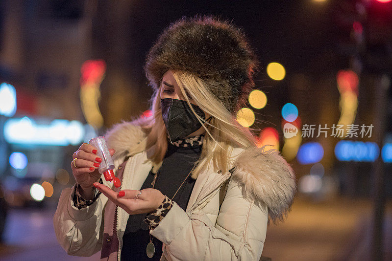 年轻女子戴着口罩等着过马路，戴着口罩的妇女等着过马路，用消毒液凝胶