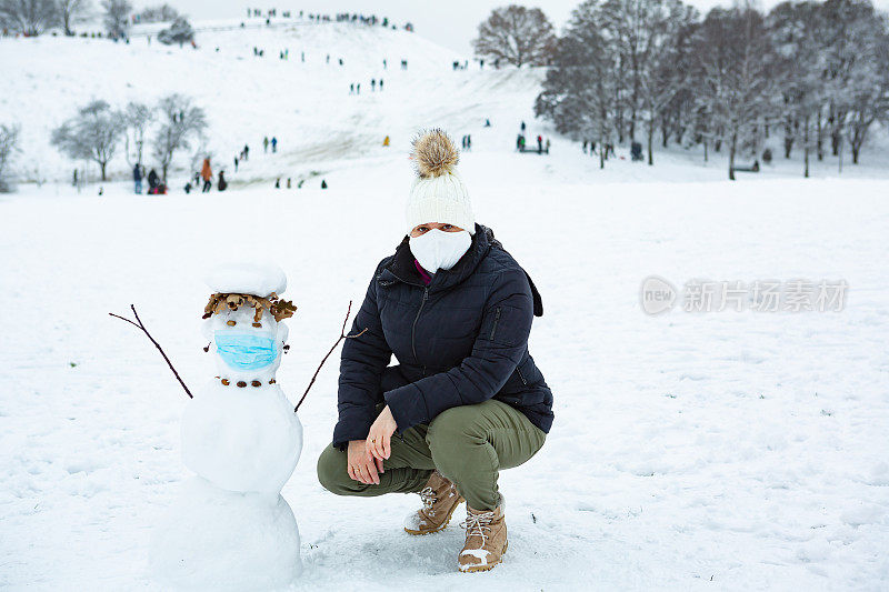 在公园里，一名女子在雪人旁边摆出蹲伏的姿势