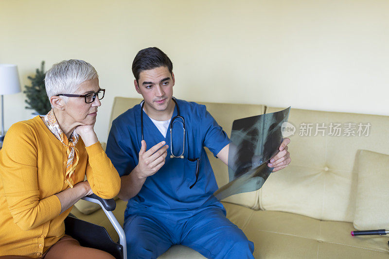 身穿蓝色制服的年轻男医生正在拜访一位坐在轮椅上的年长妇女，并在x光图像上诊断。