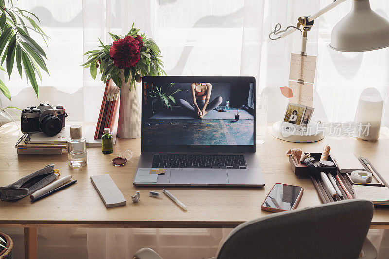 呆在家里的概念:舒适的工作区域，笔记本电脑屏幕上有一张匿名女性做瑜伽的照片