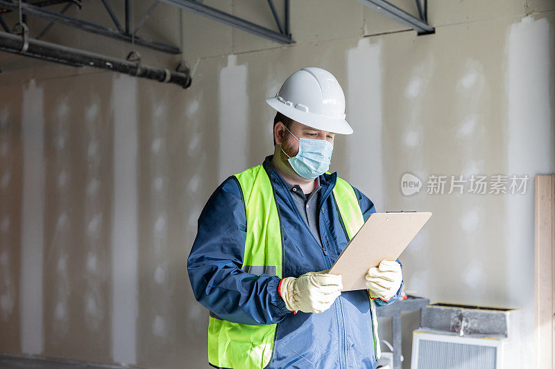 建筑工人或工程师在工地上搬运材料并查看剪贴板上的平面图