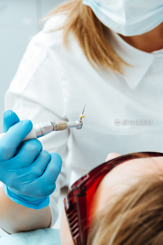 牙医戴着蓝色手套，在病人的上方拿着钻孔工具