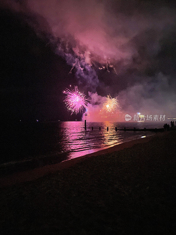 海滩烟火表演的形象从水边,浓烟和火焰在夜空反映在水中,伯恩茅斯,多塞特郡,英格兰,英国