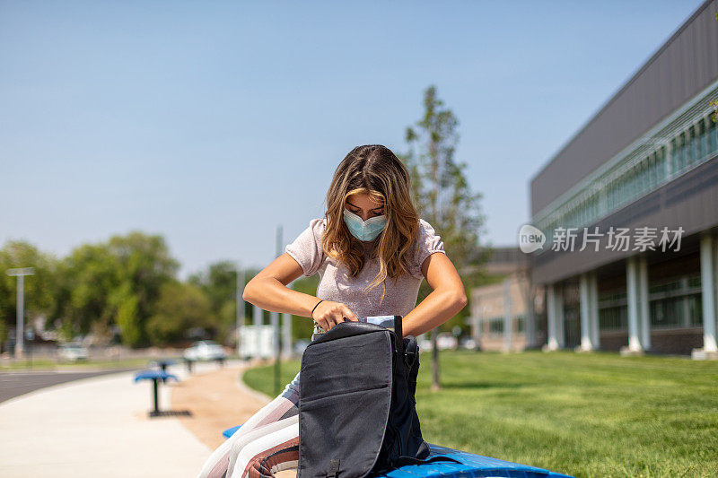 女青少年戴着口罩坐在公立学校大楼外，强制遵守重返学校照片系列