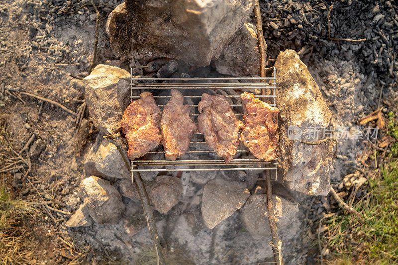 准备两块猪肉或牛排的过程。用金属便携式烧烤架烤肉，带有明亮的火焰和余烬的烧烤架