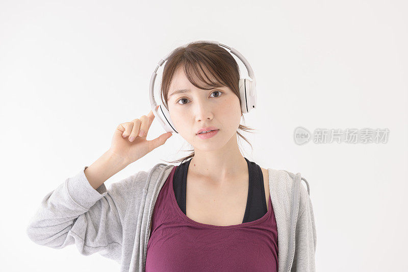 一名年轻女子站在白色背景前，戴着耳机看着前方。