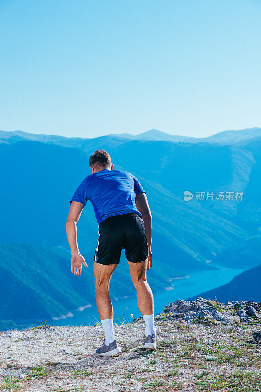 帅气的运动员穿着运动服站在悬崖边做跳跃和俯卧撑。