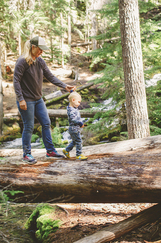 母亲帮助幼童沿着森林中的一根原木走