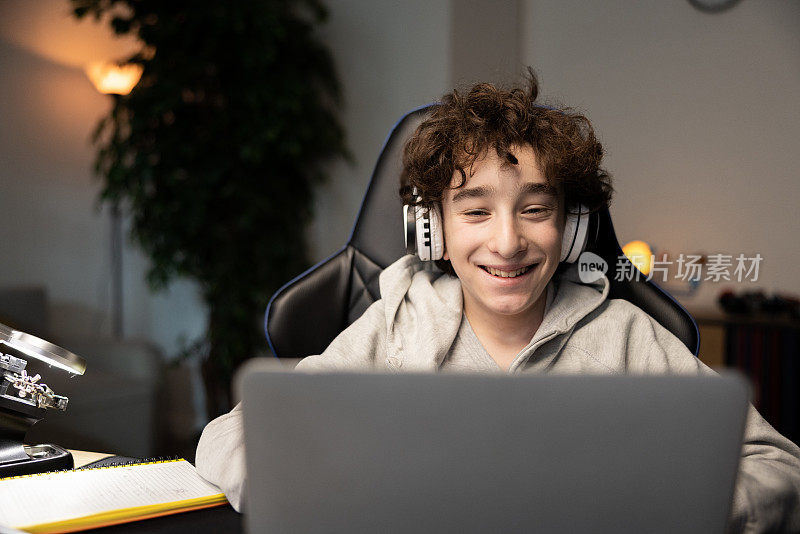 快乐的聪明的小男孩的肖像在笔记本电脑的网络摄像头微笑。孩子可以远程上课，和老师视频聊天。他正在使用无线耳机
