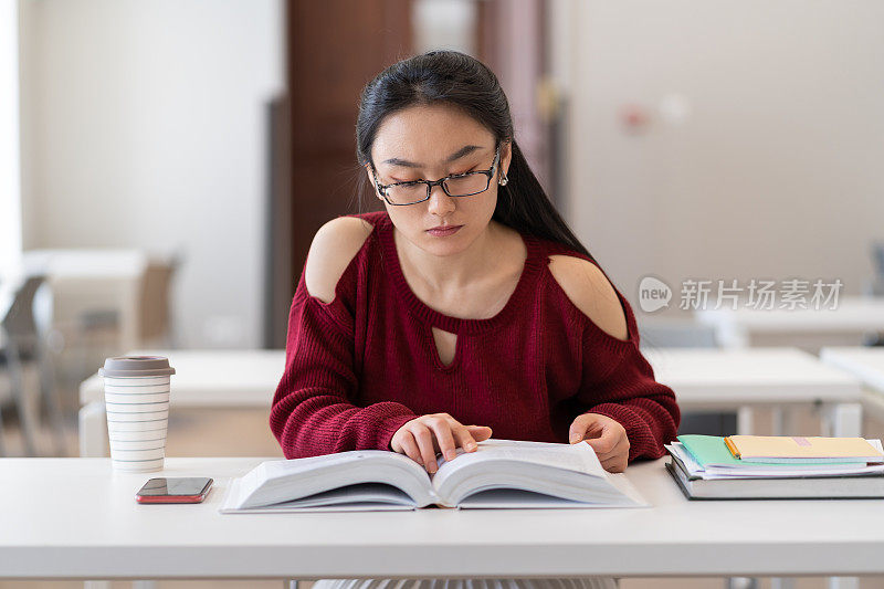 书呆子亚洲女孩阅读教科书，准备考试或测试在图书馆阅览室
