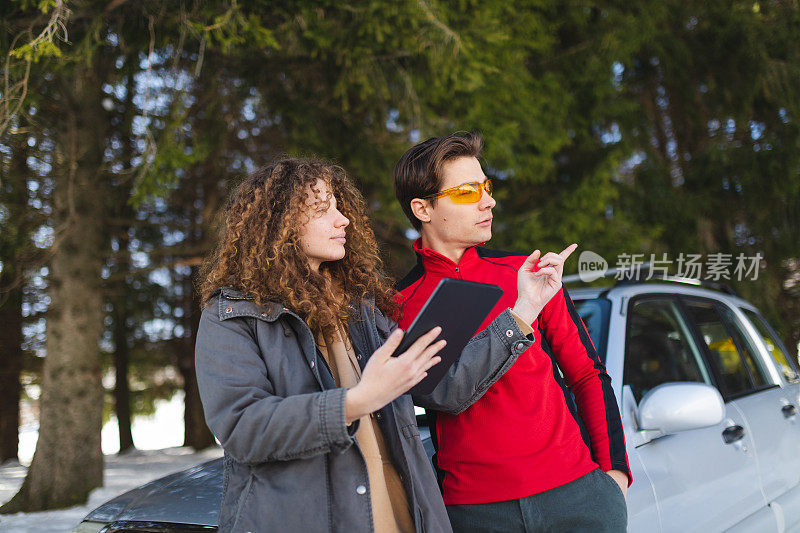 一对美丽的年轻夫妇在森林里迷了路，试图用他们的平板电脑寻找方向，背景是他们的汽车