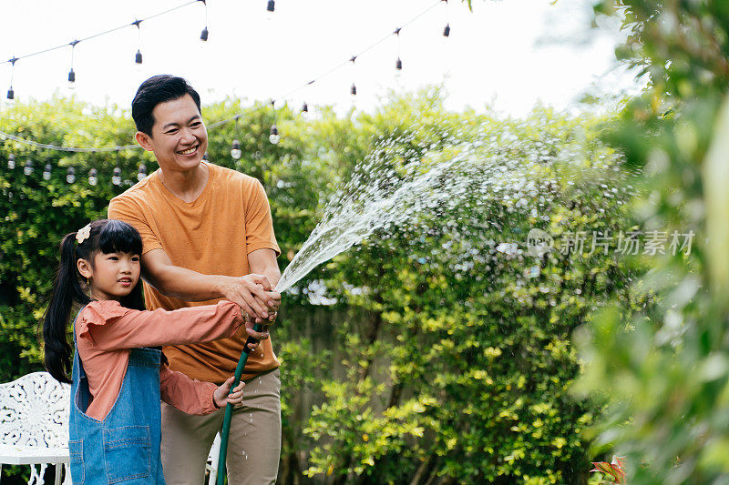 幸福的亚洲家庭的父亲和女儿在家里浇灌植物和灌木。一起在花园里度过时光