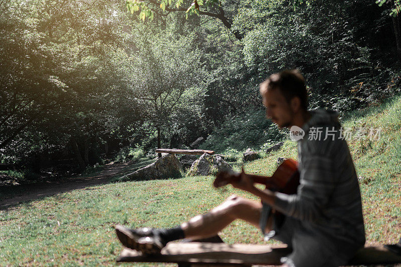 Silouette拍摄的一个年轻人坐在树木环绕的自然环境中弹吉他
