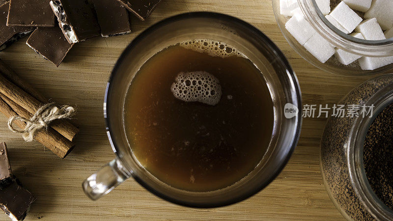 速溶咖啡制备过程的俯视图。的概念。将咖啡，方糖和热水放入木桌背景上的透明杯子，加入巧克力和肉桂。