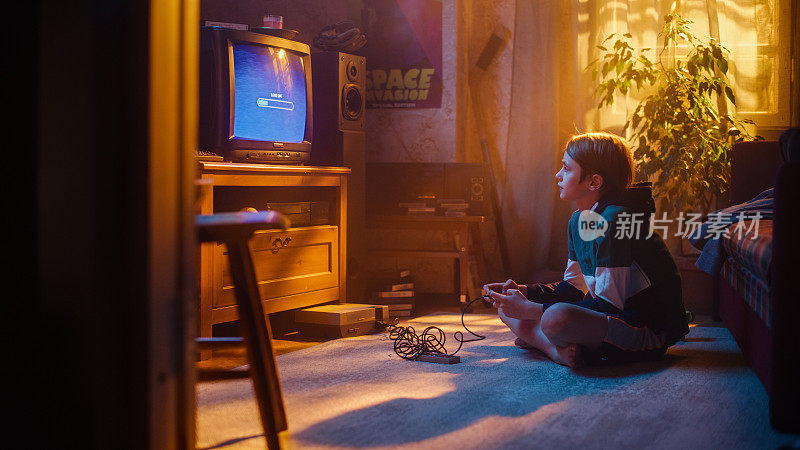 怀旧的童年概念:年轻的男孩在家里的复古电视机上玩老派街机视频游戏，房间内部的年代是正确的。孩子等待水平加载。