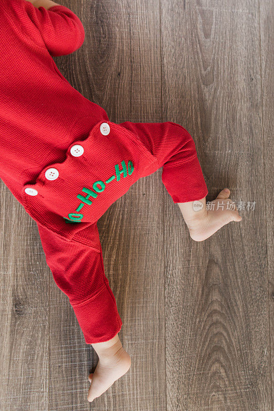 一个11个月大的圣诞宝宝穿着红色复古风格的圣诞睡衣，底部写着“HO-HO-HO”，在木地板上玩耍，为他的生日和2022年的假期做准备