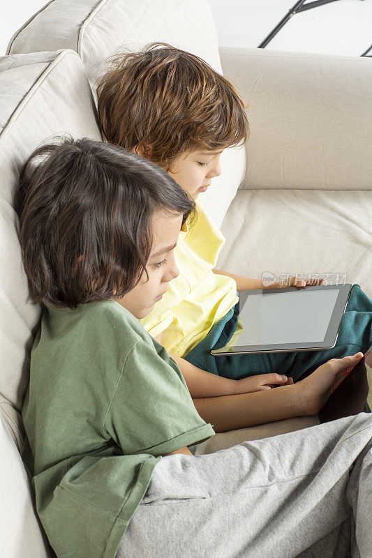 两兄弟正在沙发上玩数码平板电脑。