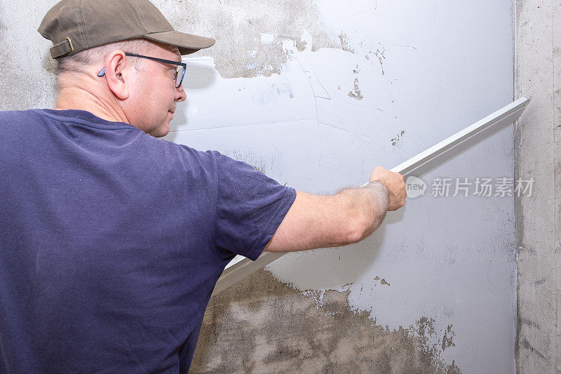 一个白种男性建筑工人正在用抹灰标尺抹平一堵灰泥墙