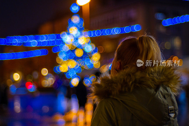 一名女子在夜晚欣赏被灯光照亮的散焦圣诞树