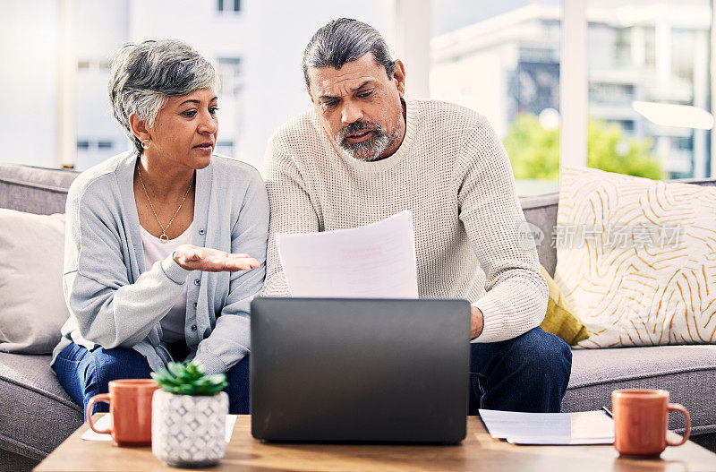 老年夫妇，文书工作和压力在笔记本电脑上与财务文件，税务或退休问题在家里。规划债务、电脑和沙发上的人的人寿保险、账单或资产管理