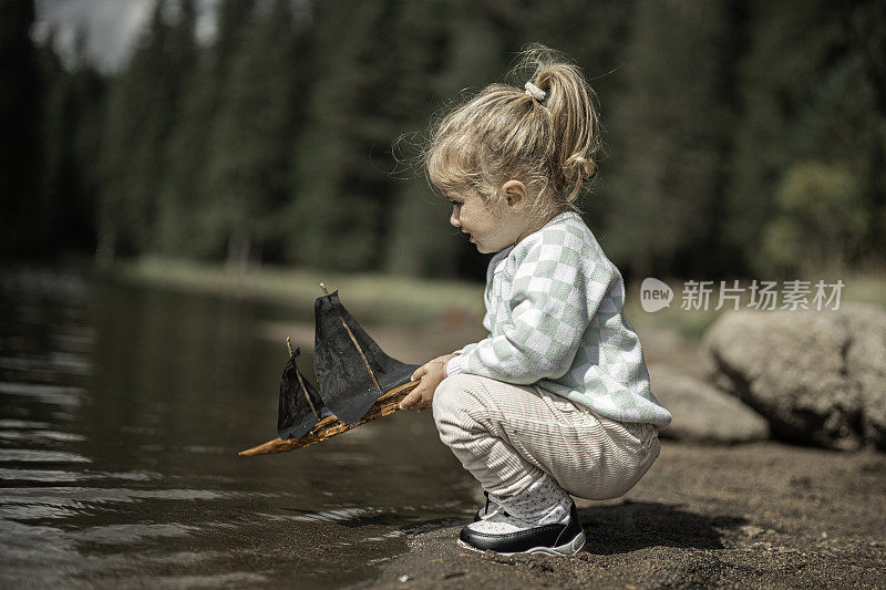 女孩在湖边玩玩具帆船。