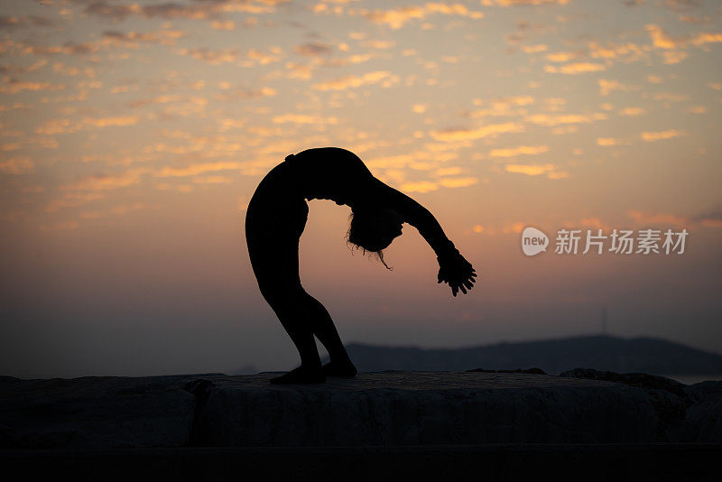 夕阳下柔韧的年轻女子剪影。