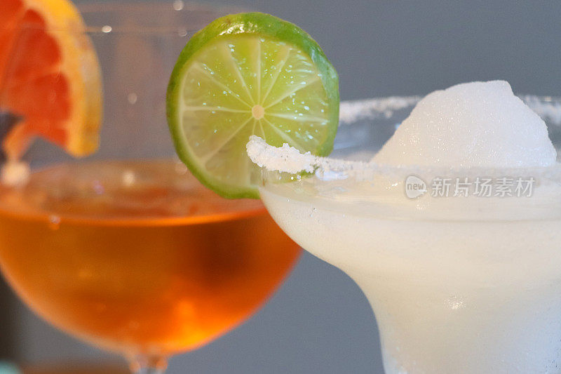 两种鸡尾酒的特写图片，斯普里茨威尼斯和冷冻玛格丽塔龙舌兰为基础的鸡尾酒饮料装饰橘子和酸橙片，盐边的玛格丽塔玻璃杯，重点在前景