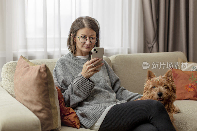 年轻的成年女子坐在客厅的沙发上玩手机