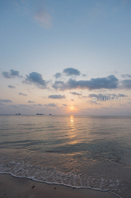 太阳落在宁静的海面上，在柔和的天空下，沿着水面投射出温暖的光芒和柔和的倒影