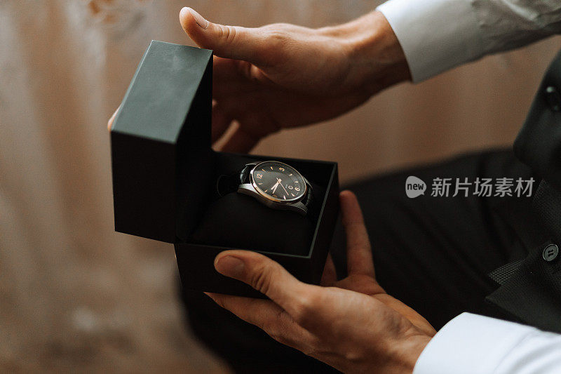 一个穿着昂贵的经典西装的男人看着手表的特写镜头。一个男人拆开礼物。一个英俊的男人，手里拿着一块珍贵的手表。
