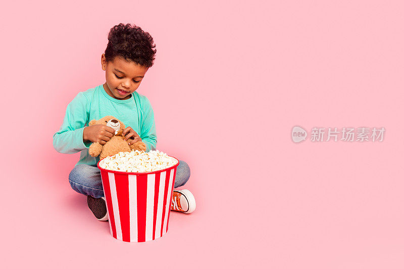 迷人的小男孩的全尺寸照片坐在地板上玩泰迪熊爆米花穿时髦的海蓝宝石服装孤立在粉红色的背景