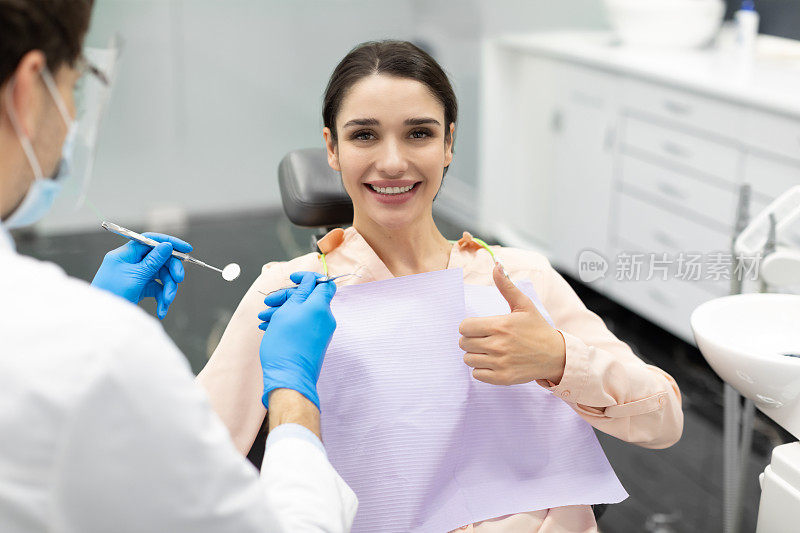 女病人在现代口腔诊所接受男牙医检查时，开心地竖起大拇指，享受优质的牙科治疗和医疗服务