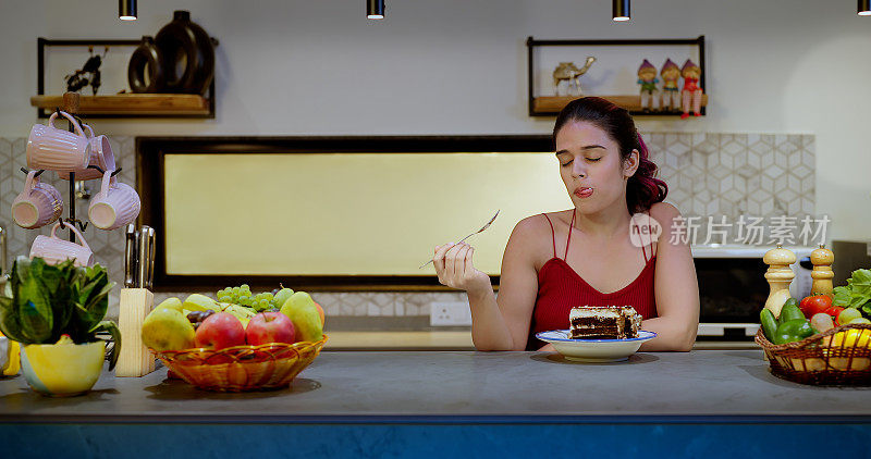印度微笑的年轻成年女子站在现代家庭厨房里，在室内吃糕点。快乐美丽可爱的z世代女性庆祝生日，享受快乐的假期