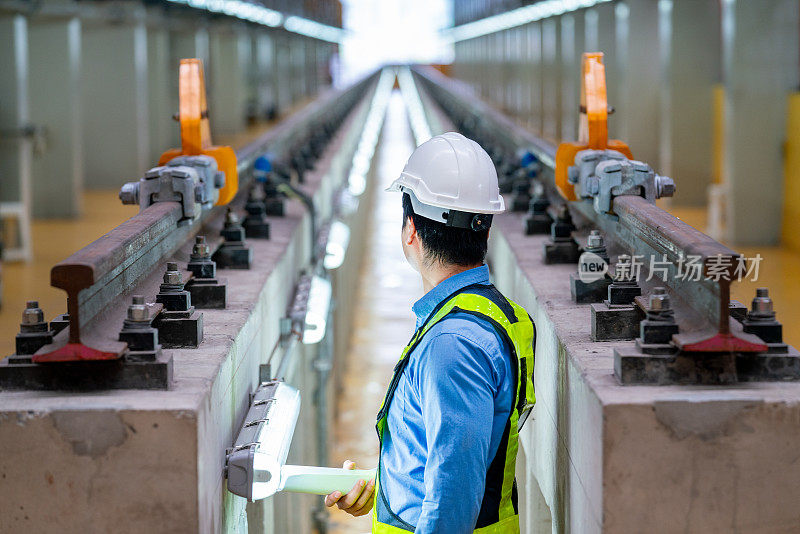 专业工程师站在电气或空轨列车的铁轨之间，看着工厂工作场所的铁轨末端。