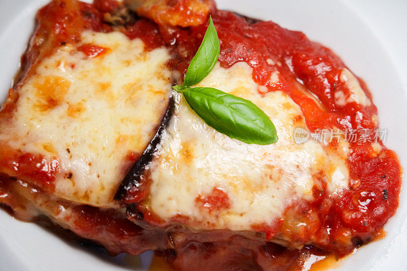 一盘美味的千层面，上面有融化的马苏里拉奶酪和一小枝罗勒和意大利番茄酱