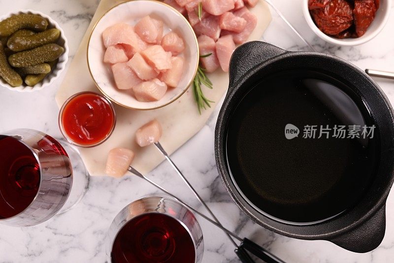 火锅锅用油、叉子、生肉块、红酒等产品放在白色大理石桌上，平铺
