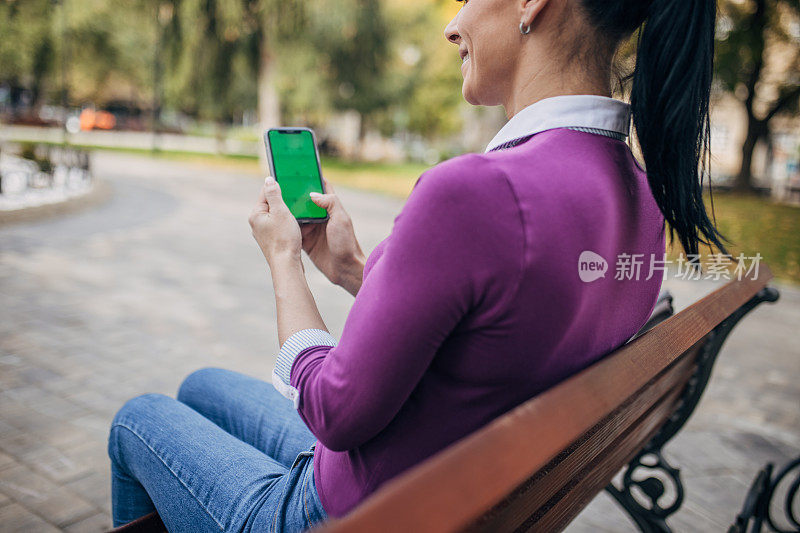 一个女人坐在公园的长椅上玩智能手机