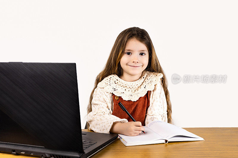快乐的小女孩在桌子上有笔记本电脑和笔记本