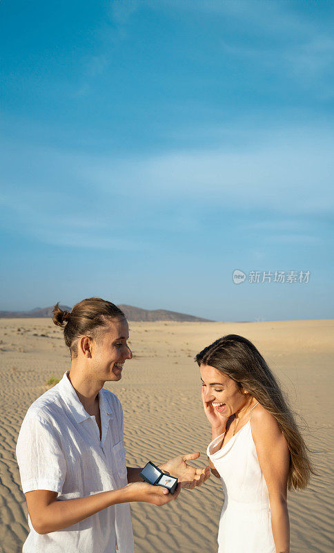 在蓝天下的沙滩上，快乐的女人被伴侣的求婚惊呆了