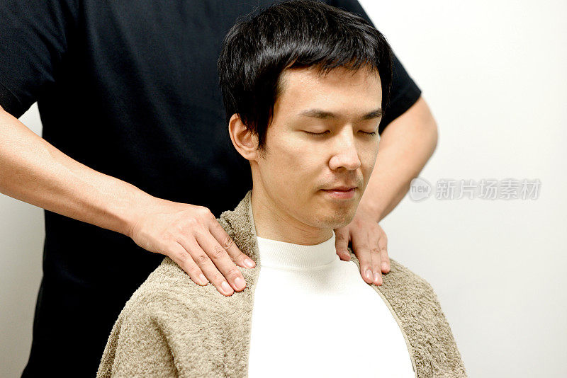 一名亚洲男子正在接受脊椎按摩师的肩部按摩