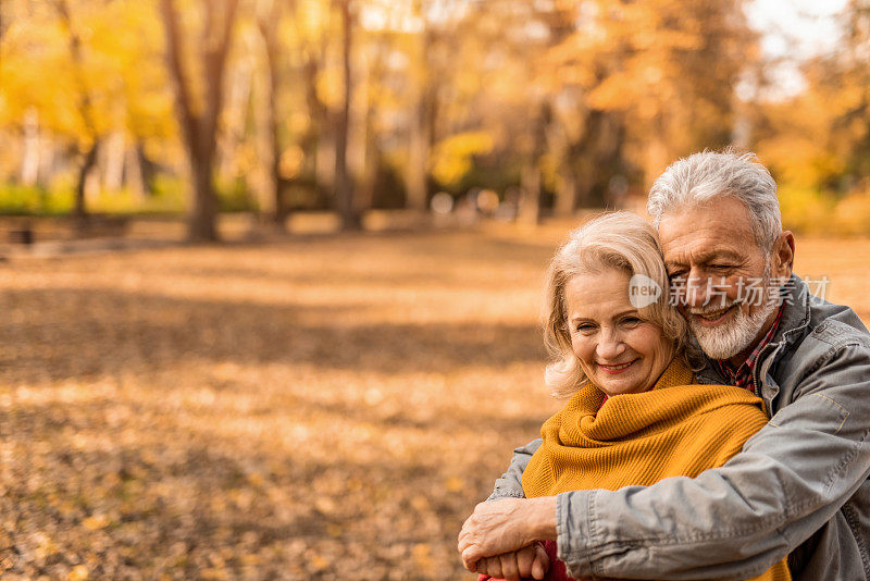 秋日，一对浪漫的老年情侣站在公园里拥抱。