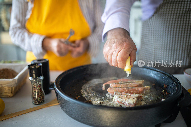 老男人在家里和妻子一起做饭时在鱼上挤柠檬汁