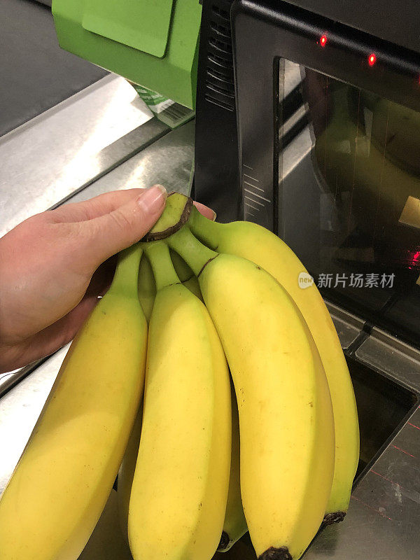 一个不知名的人拿着一串香蕉在超市自助结账处扫描(自助结账)